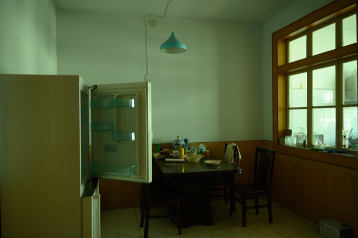 Green light in a quiet room, with an open refrigerator, a hanging lamp and a wooden table.